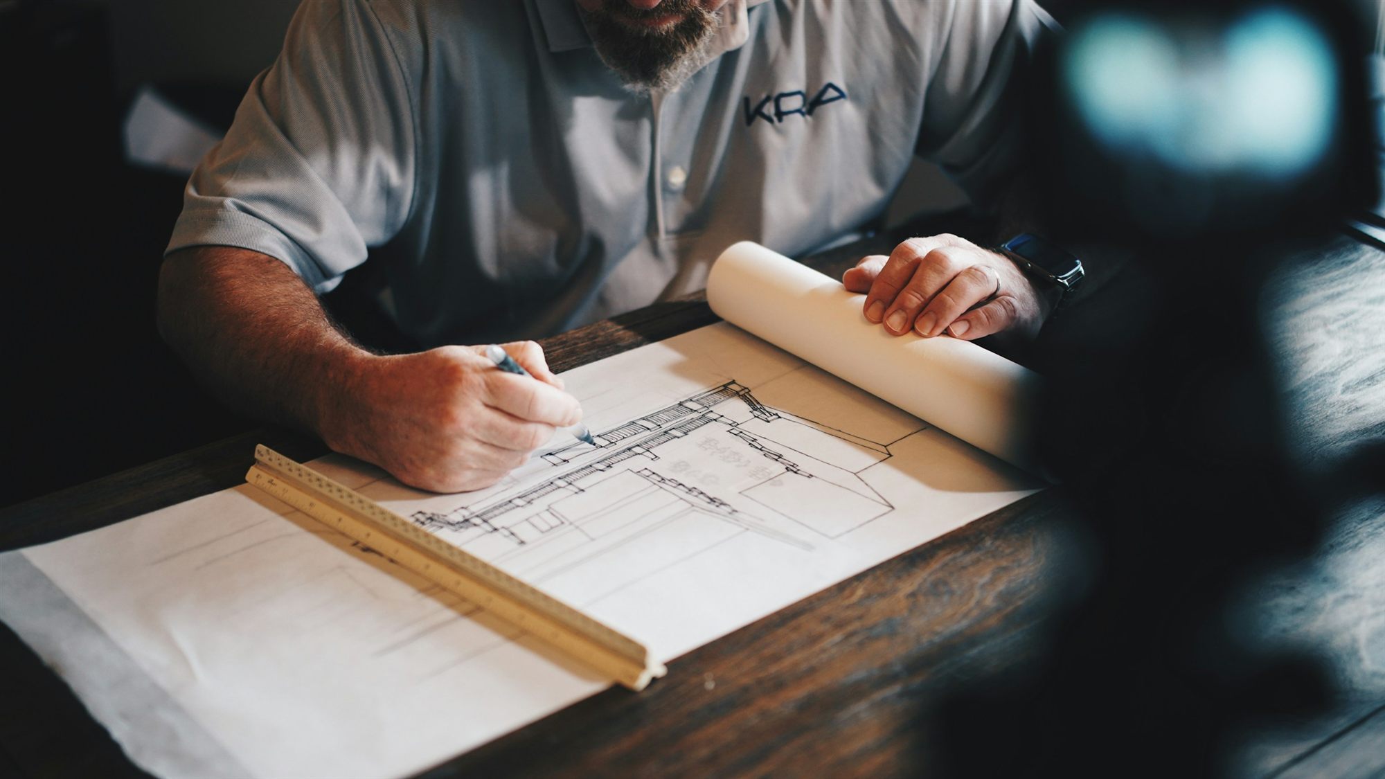 Manos de un arquitecto dibujando sobre un plano con regla y lápiz.